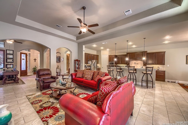 living room featuring arched walkways, ceiling fan, a raised ceiling, and visible vents