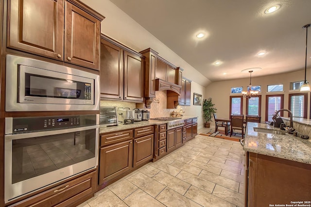 kitchen with appliances with stainless steel finishes, a sink, light stone countertops, pendant lighting, and backsplash