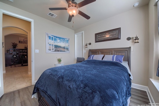 bedroom featuring arched walkways, wood finished floors, a ceiling fan, visible vents, and baseboards