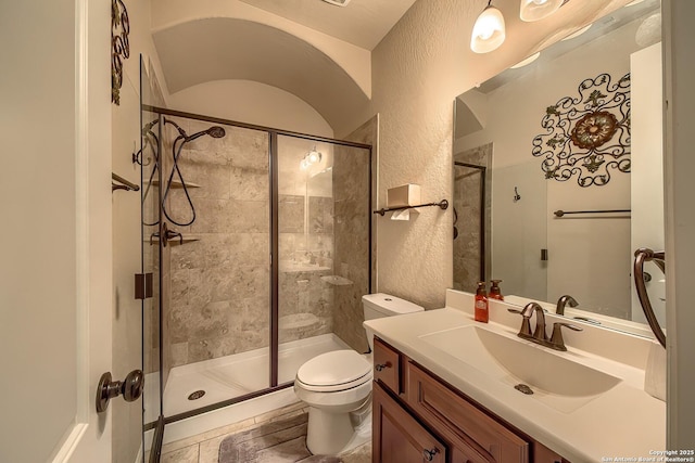 bathroom featuring a textured wall, a stall shower, vanity, and toilet