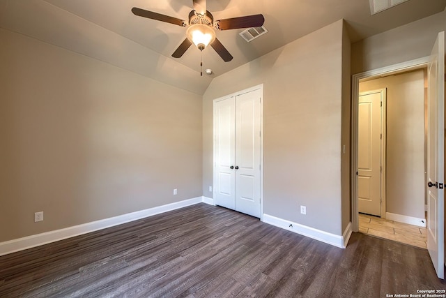 unfurnished bedroom with baseboards, visible vents, dark wood finished floors, vaulted ceiling, and a closet