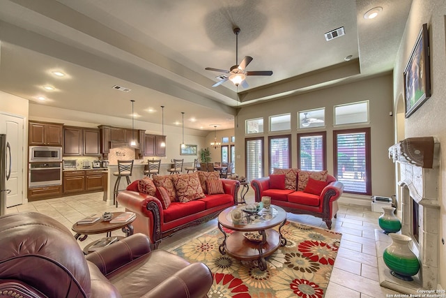 living room featuring a fireplace with raised hearth, a raised ceiling, visible vents, and a healthy amount of sunlight