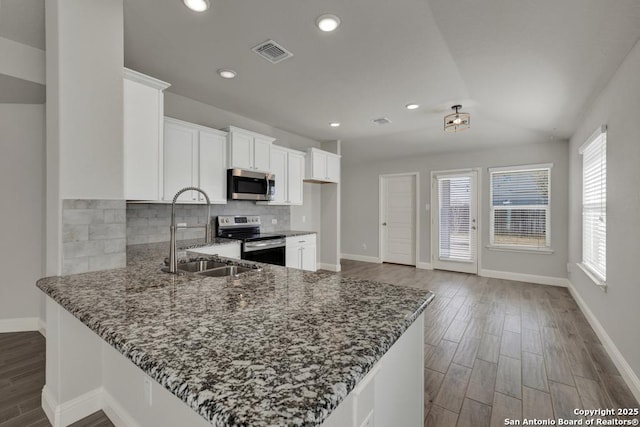 kitchen with visible vents, dark stone counters, appliances with stainless steel finishes, a sink, and backsplash