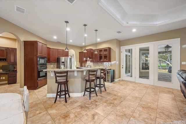 kitchen featuring a breakfast bar, visible vents, backsplash, under cabinet range hood, and black appliances