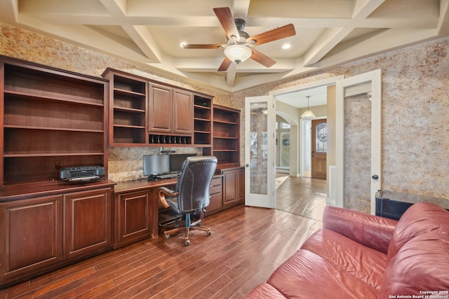 office area with arched walkways, dark wood-style flooring, coffered ceiling, built in desk, and wallpapered walls