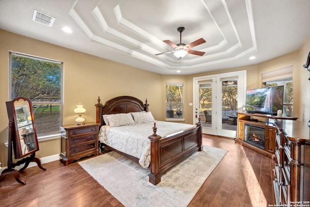 bedroom featuring a tray ceiling, wood finished floors, visible vents, and access to exterior