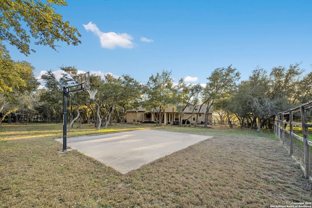 view of basketball court featuring basketball hoop, a yard, and fence