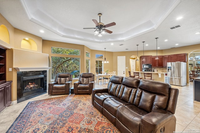 living area with a fireplace with flush hearth, a tray ceiling, visible vents, and arched walkways