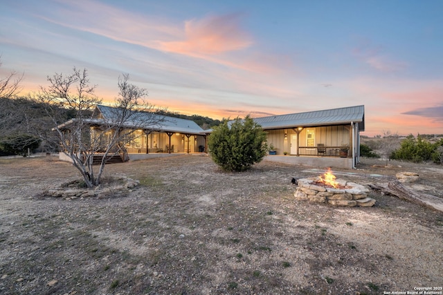 back of property at dusk with a fire pit, metal roof, and board and batten siding