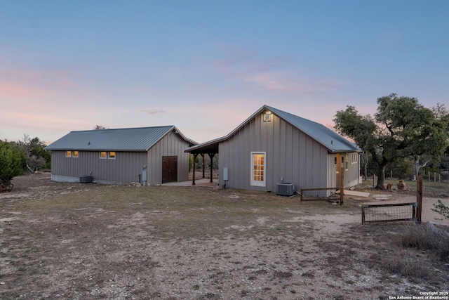 back of property at dusk featuring board and batten siding, central AC, metal roof, and an outdoor structure