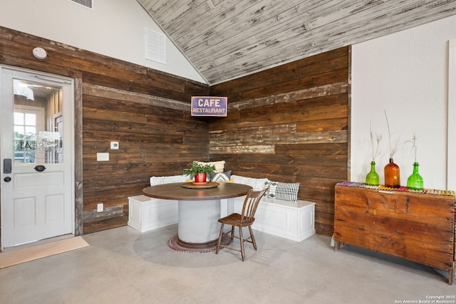 dining room featuring high vaulted ceiling, wooden ceiling, concrete floors, and wooden walls