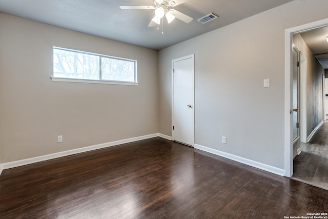 empty room with dark wood-style floors, visible vents, ceiling fan, and baseboards