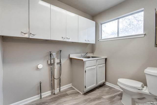 half bath with toilet, baseboards, and a sink