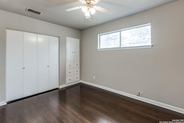 unfurnished bedroom with dark wood-style flooring, a closet, visible vents, a ceiling fan, and baseboards