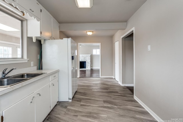 kitchen with a fireplace, light countertops, white cabinets, a sink, and white fridge with ice dispenser