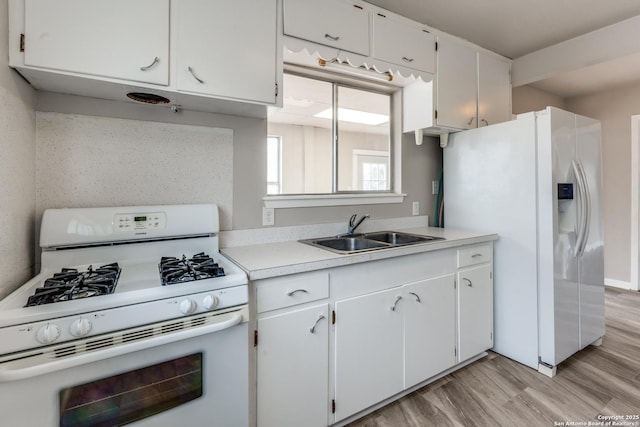 kitchen featuring light wood finished floors, light countertops, white cabinets, a sink, and white appliances