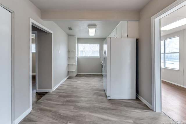 kitchen with light wood finished floors, visible vents, freestanding refrigerator, white cabinets, and baseboards