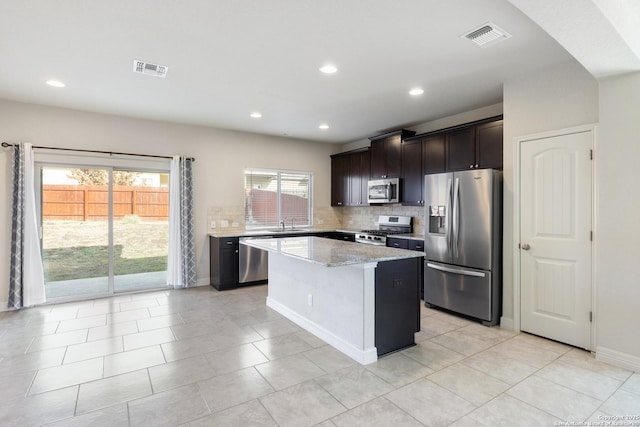 kitchen featuring stainless steel appliances, visible vents, decorative backsplash, a kitchen island, and light stone countertops