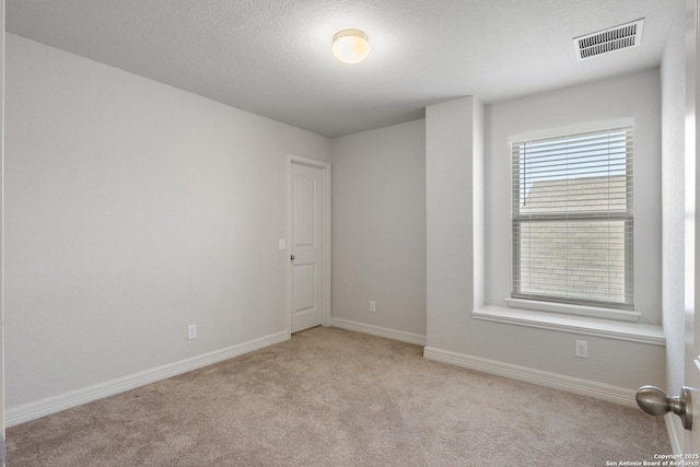 spare room featuring a textured ceiling, carpet, visible vents, and baseboards