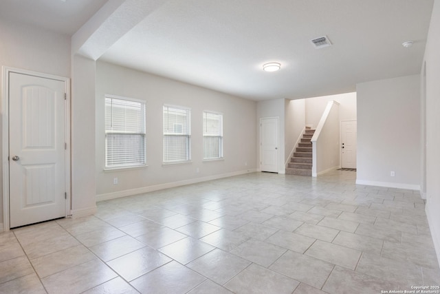 empty room with light tile patterned floors, stairway, visible vents, and baseboards