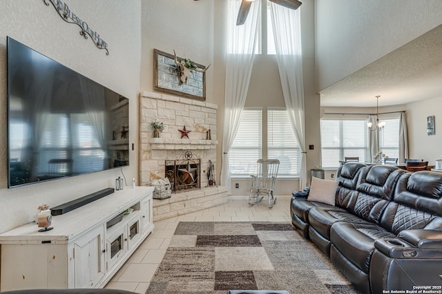 living room featuring light tile patterned floors, a high ceiling, a textured ceiling, a fireplace, and ceiling fan with notable chandelier