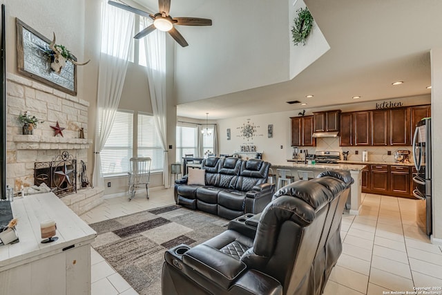 living room featuring ceiling fan, a stone fireplace, light tile patterned flooring, recessed lighting, and a towering ceiling