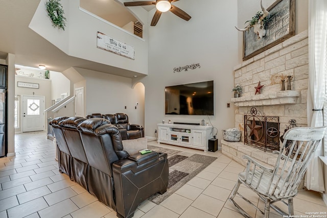 living area with light tile patterned floors, arched walkways, a high ceiling, a fireplace, and a ceiling fan