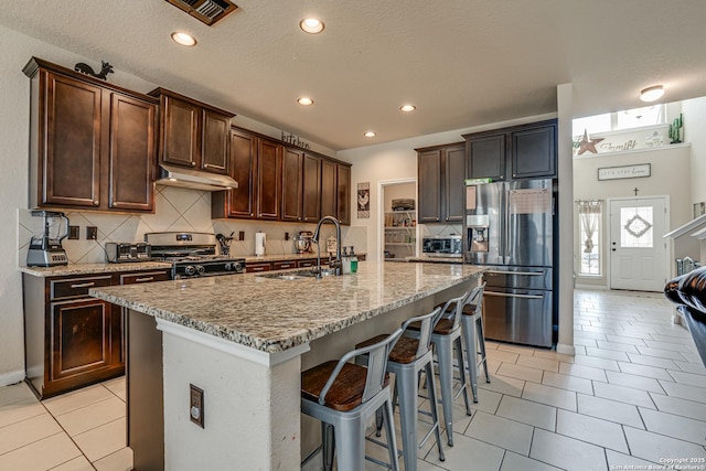 kitchen with visible vents, appliances with stainless steel finishes, light stone counters, under cabinet range hood, and a sink