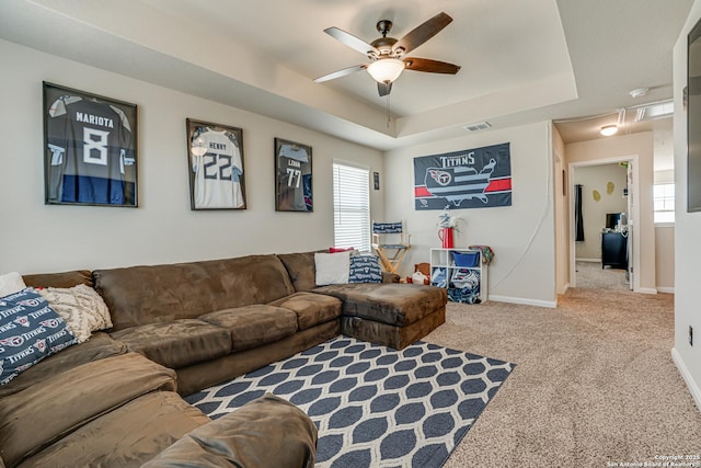 carpeted living room with visible vents, a ceiling fan, baseboards, a tray ceiling, and attic access