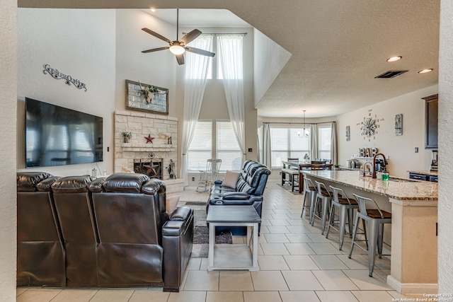 living room with light tile patterned floors, visible vents, a ceiling fan, a textured ceiling, and a stone fireplace