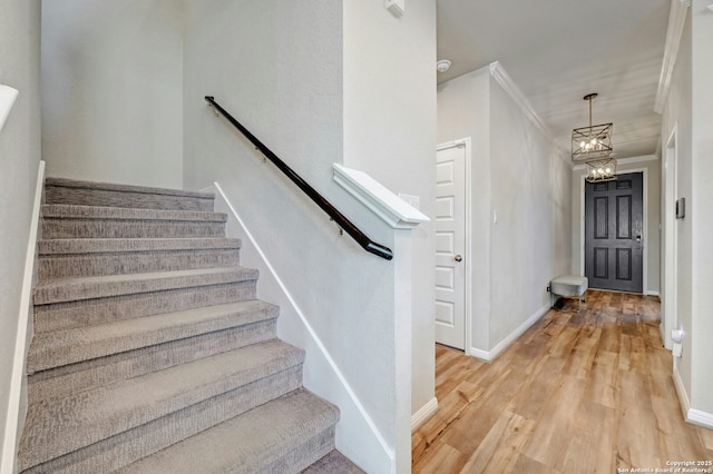 stairway featuring baseboards, an inviting chandelier, wood finished floors, and crown molding