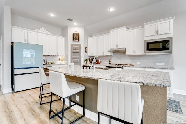 kitchen with under cabinet range hood, built in microwave, white cabinets, and freestanding refrigerator