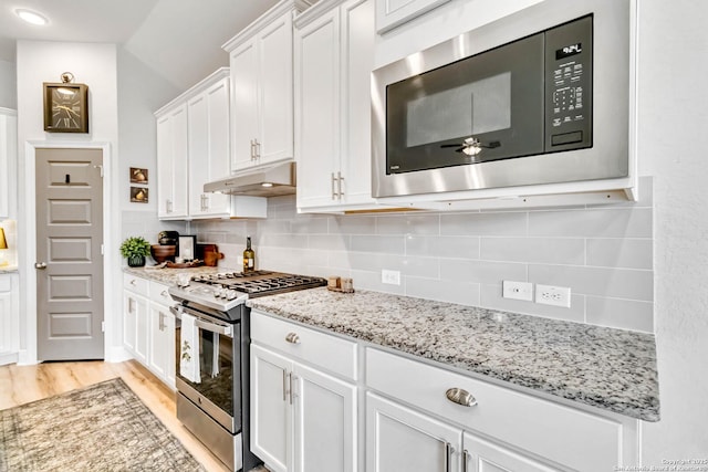 kitchen featuring white cabinets, under cabinet range hood, tasteful backsplash, and stainless steel appliances