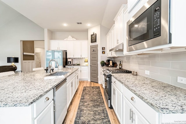 kitchen with white cabinets, stainless steel appliances, light wood-type flooring, under cabinet range hood, and a sink