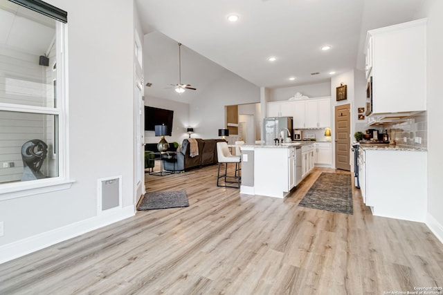 kitchen featuring light wood finished floors, open floor plan, a kitchen breakfast bar, white cabinetry, and gas range gas stove