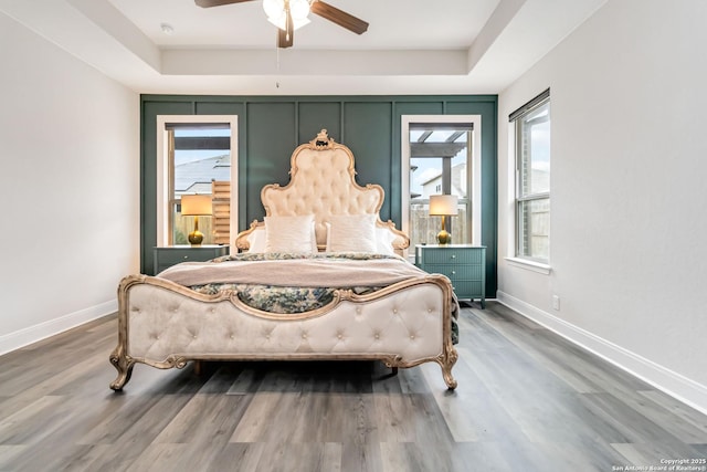 bedroom with a tray ceiling, ceiling fan, baseboards, and wood finished floors