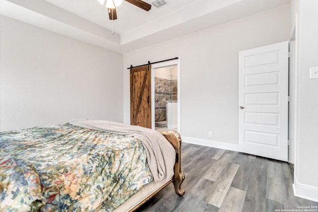 bedroom featuring a tray ceiling, a barn door, baseboards, and wood finished floors