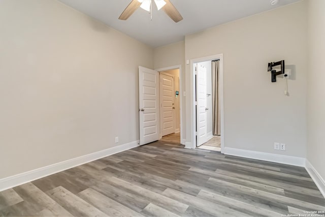 unfurnished bedroom featuring a ceiling fan, ensuite bath, baseboards, and wood finished floors