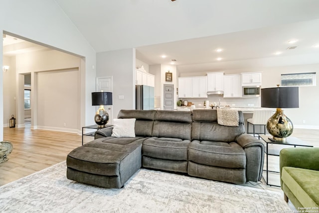 living room with lofted ceiling, recessed lighting, light wood-type flooring, and baseboards