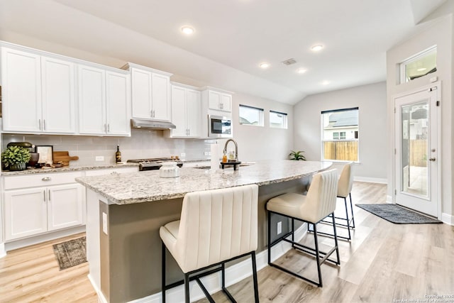 kitchen featuring under cabinet range hood, a sink, visible vents, decorative backsplash, and stainless steel microwave