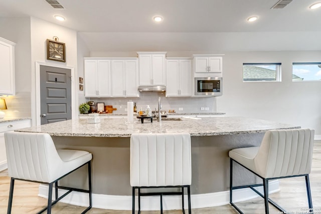 kitchen featuring white cabinetry, under cabinet range hood, visible vents, and stainless steel microwave