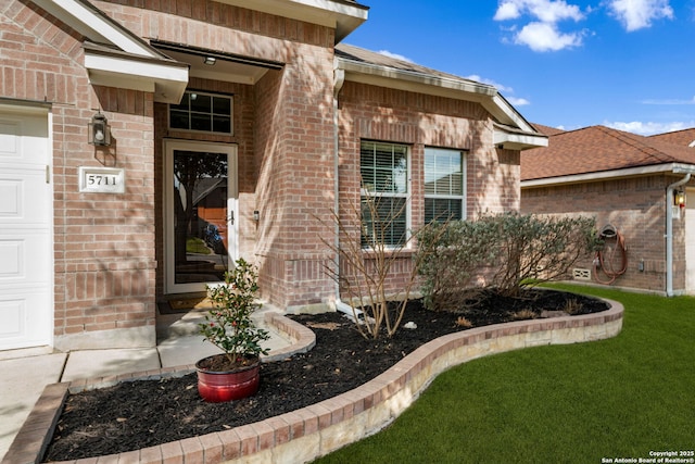 view of exterior entry with a garage, brick siding, and a shingled roof