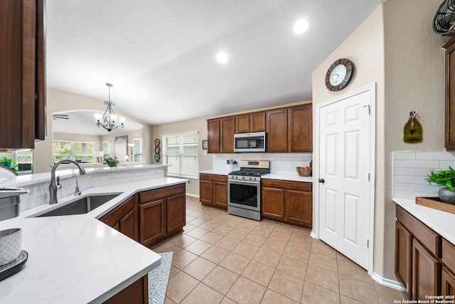 kitchen with a sink, vaulted ceiling, light countertops, appliances with stainless steel finishes, and decorative backsplash