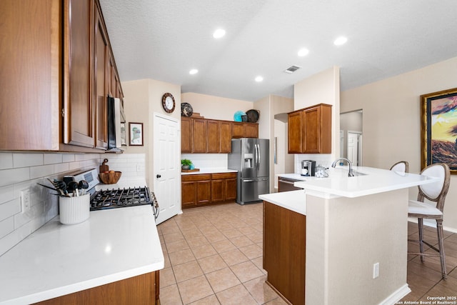 kitchen with a peninsula, visible vents, appliances with stainless steel finishes, brown cabinetry, and a kitchen bar