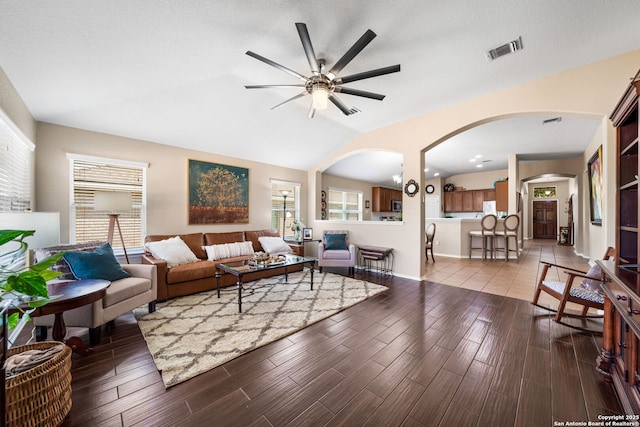 living area with arched walkways, visible vents, dark wood-type flooring, vaulted ceiling, and ceiling fan