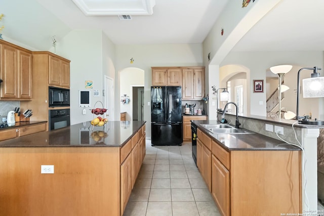 846 County Road 2763, Mico, TX 78056 - kitchen featuring arched walkways, light tile patterned floors, a sink, black appliances, and an island with sink