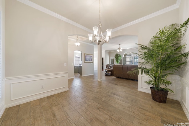 interior space featuring arched walkways, crown molding, a decorative wall, and wood finished floors