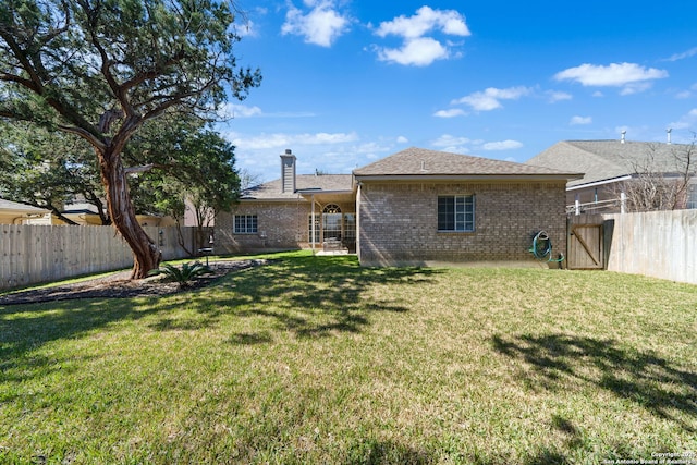 back of house with brick siding, fence, a chimney, and a lawn