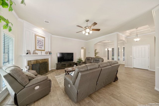 living area featuring visible vents, arched walkways, a tiled fireplace, ornamental molding, and light wood-type flooring