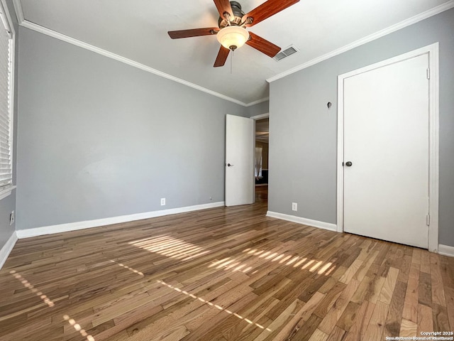 unfurnished bedroom featuring baseboards, visible vents, a ceiling fan, ornamental molding, and wood finished floors